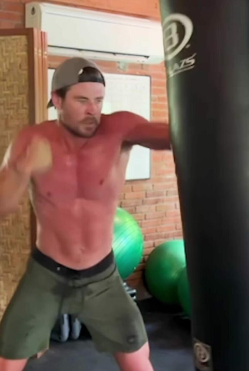 Chris Hemsworth actor haciendo ejercicio con shorts verdes sin playera costal de boxeo.