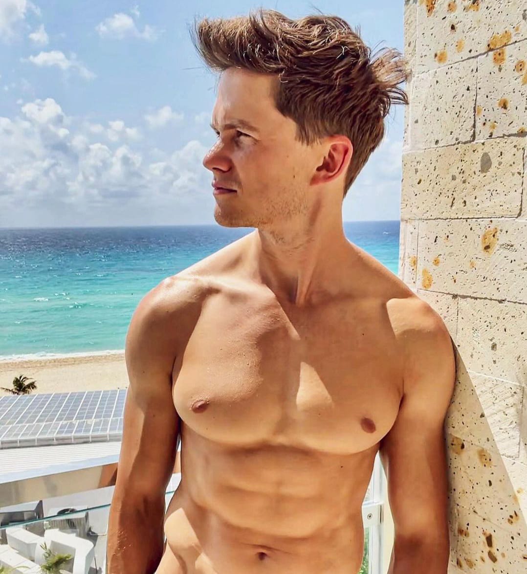 Actor Tom Prior sin playera en la playa